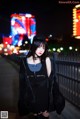 A woman in a black dress and hat standing on a bridge.