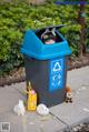 A person in a trash can with two rabbits and a stuffed animal.