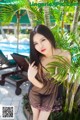 A woman in a black dress posing by a pool.