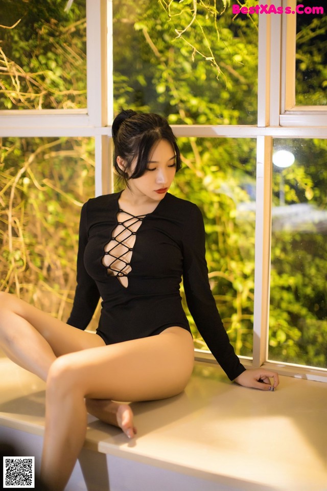 A woman in a black bodysuit sitting on a window sill.