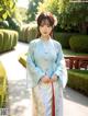 A woman in a blue and white hanbok standing in a garden.