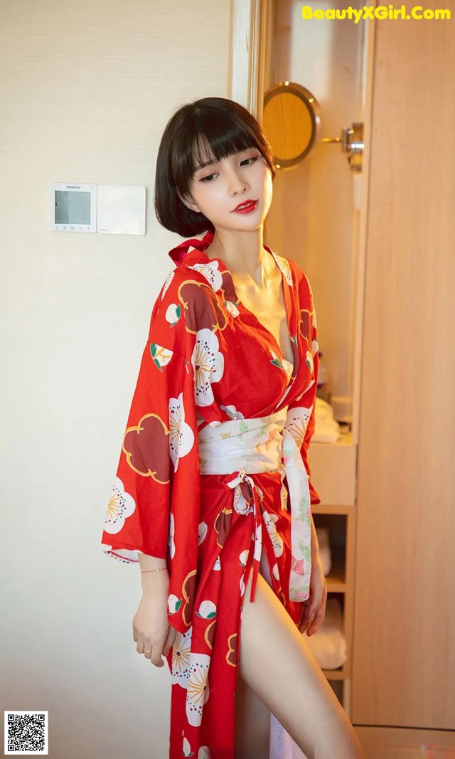 A woman in a red kimono standing in front of a mirror.