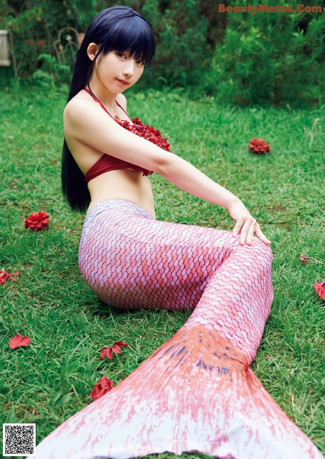 A woman in a mermaid tail sitting on the grass.