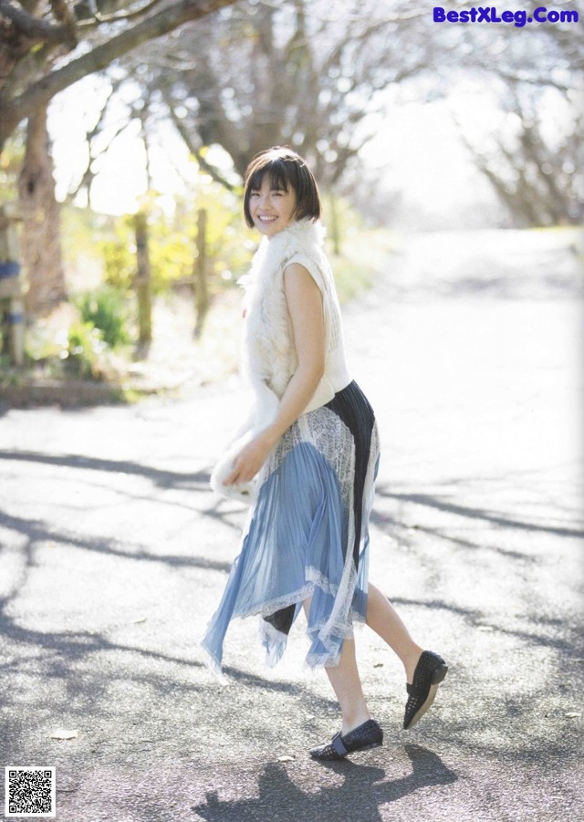 A woman walking down a street in a blue skirt.